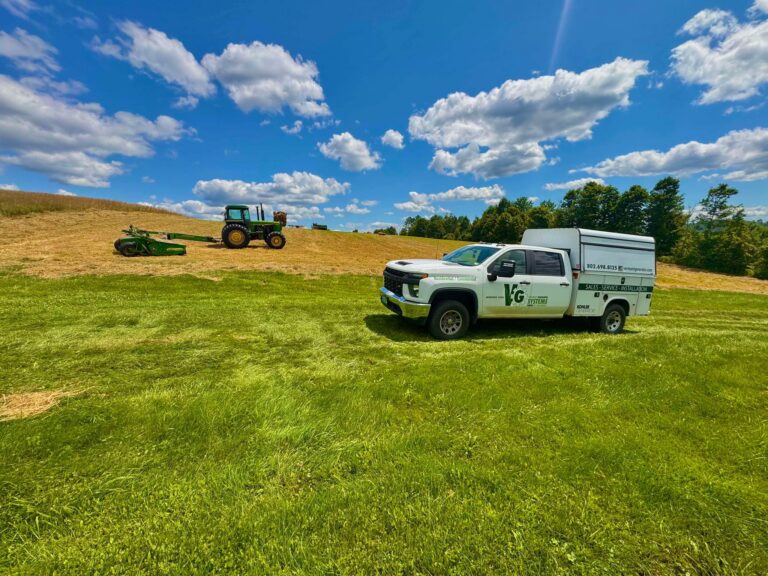 White Vermont Generator Systems tuck parked in a field with a tractor in the background.